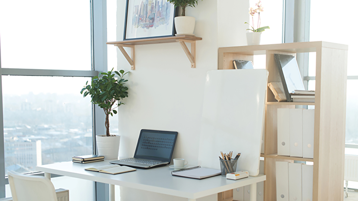 Aufgeräumter Schreibtisch dank digitaler Archivierung mit Laptop mittig und Pflanze auf der linken Seite
